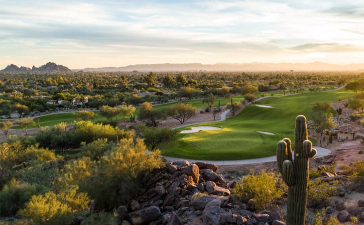 A green golf course is surrounded by saguaro cactus and mountains