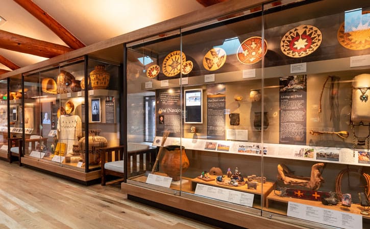 Woven baskets and traditional indigenous costumes are displayed in glass cases alongside other handcrafted goods and tools