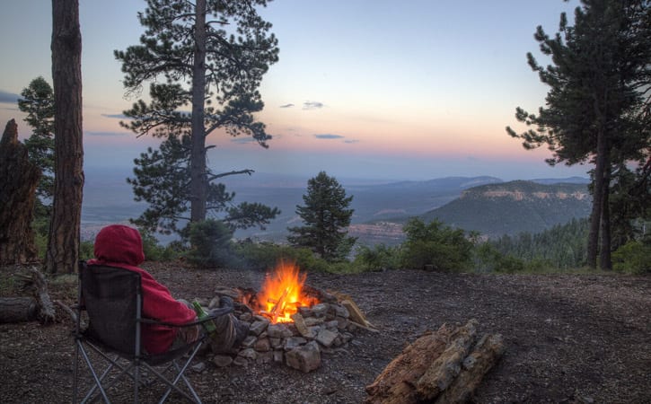 A man sits near a small campfire overlooking the Grand Canyon