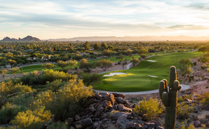 A green golf course is surrounded by saguaro cactus and mountains