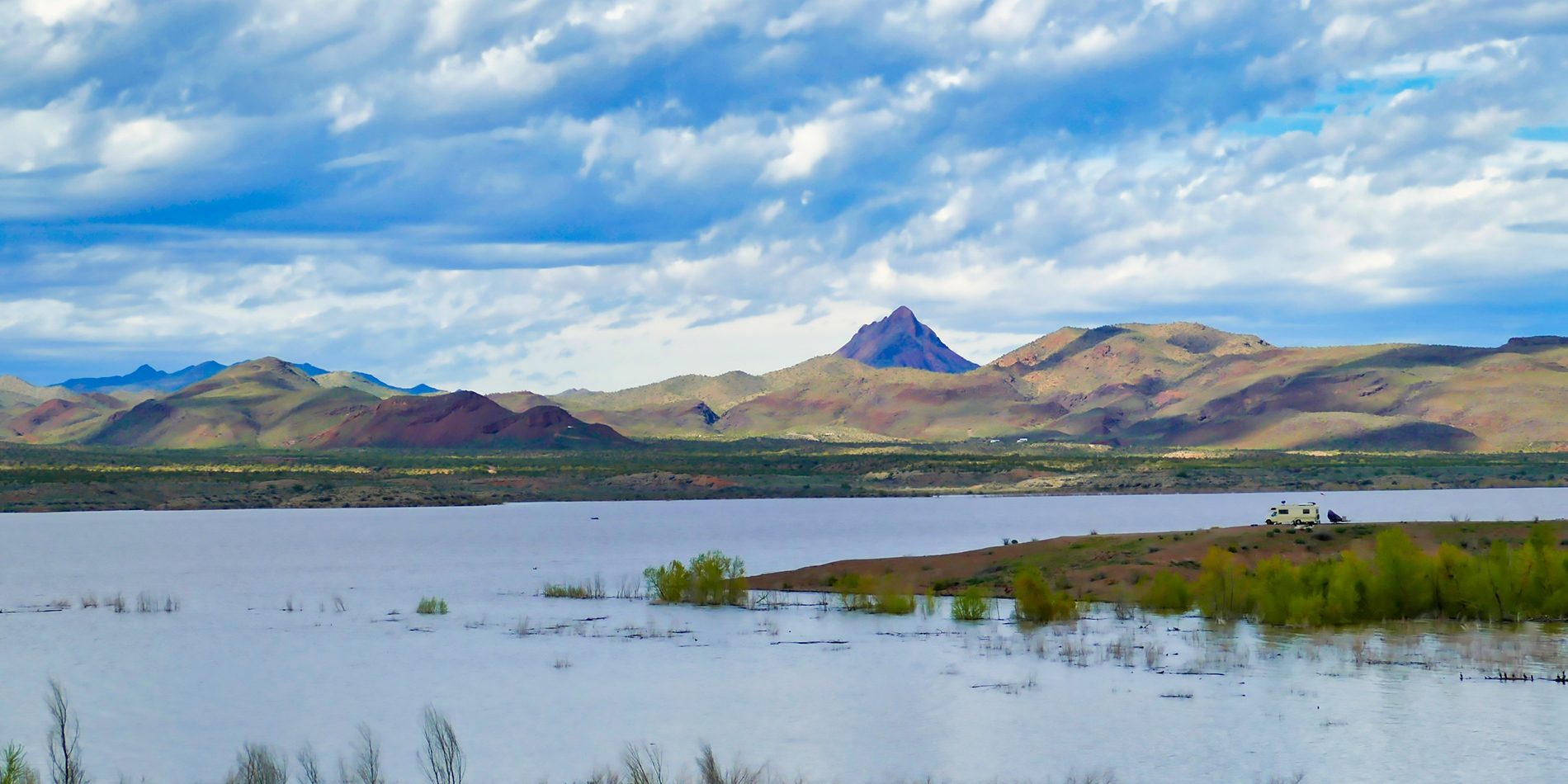 Landscape of Alamo Lake. Lake in the foreground with rolling hills in the background and a motorhome parked near the waters edge.